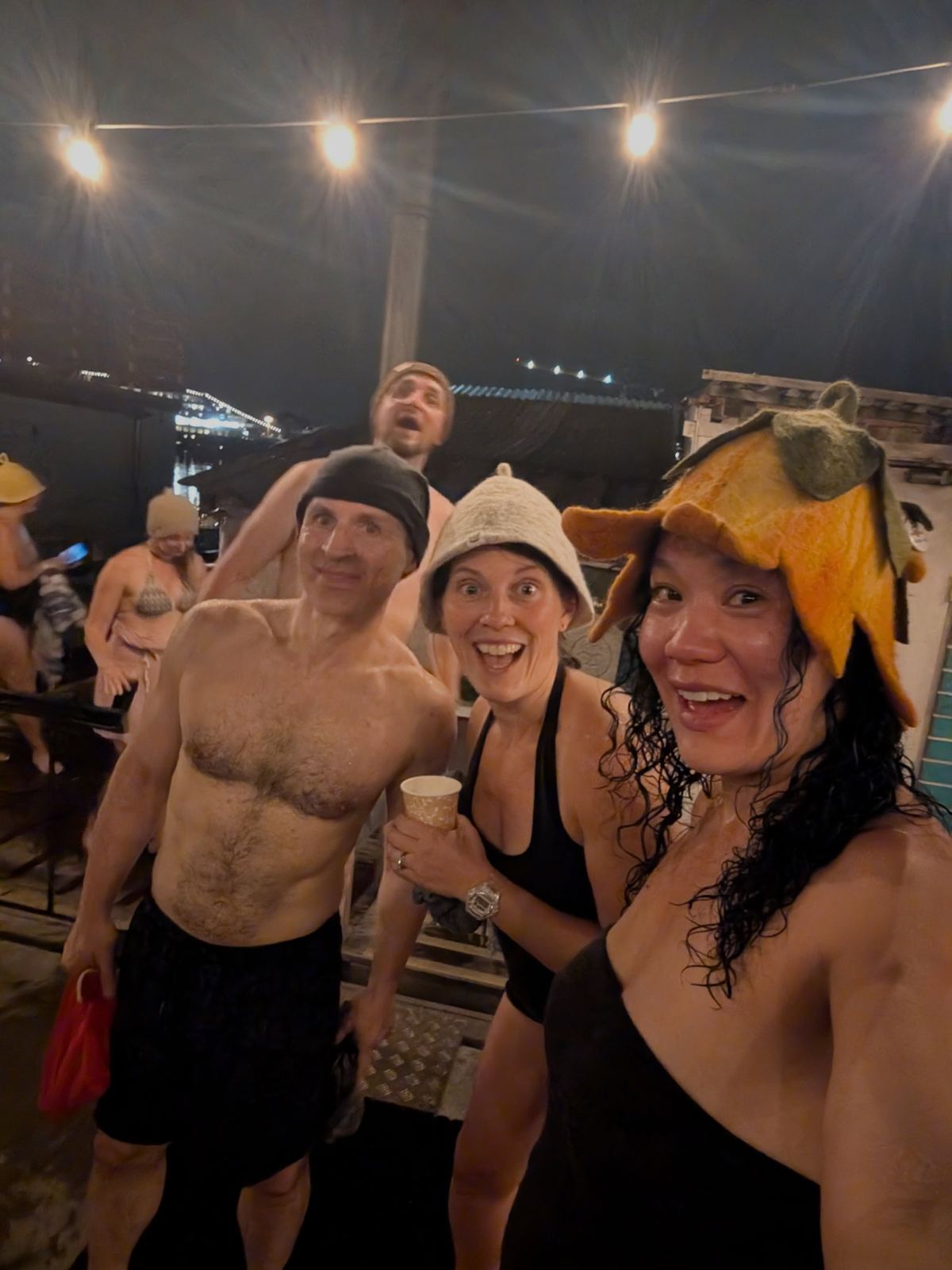 Bathers in sauna hats laughing on a harbour sauna deck at night